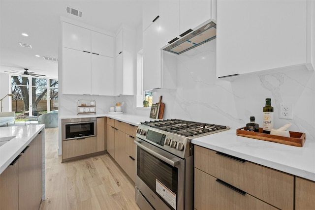 kitchen featuring built in microwave, tasteful backsplash, high end range, extractor fan, and white cabinets