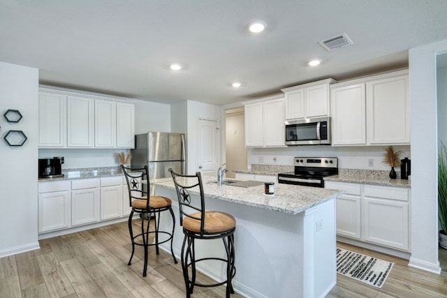 kitchen with appliances with stainless steel finishes, light stone counters, a center island with sink, light hardwood / wood-style floors, and white cabinetry