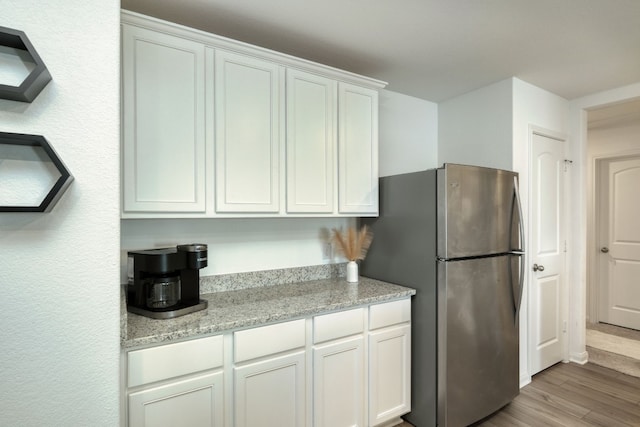 kitchen featuring stainless steel fridge, white cabinets, light stone countertops, and light hardwood / wood-style floors