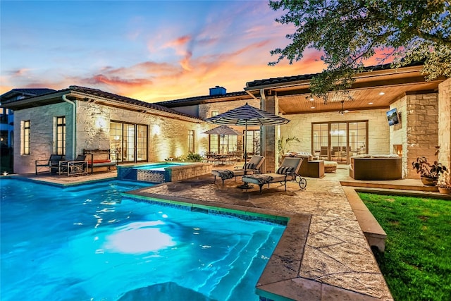 pool at dusk featuring an in ground hot tub, a patio, and an outdoor living space