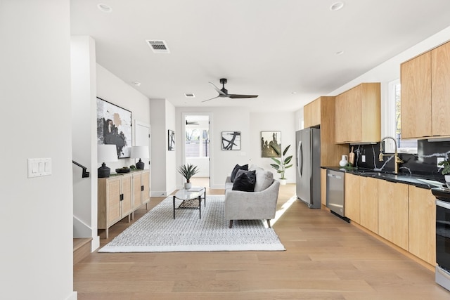 kitchen with sink, light hardwood / wood-style flooring, ceiling fan, appliances with stainless steel finishes, and backsplash