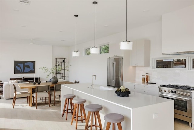 kitchen with a center island with sink, premium appliances, white cabinetry, and tasteful backsplash