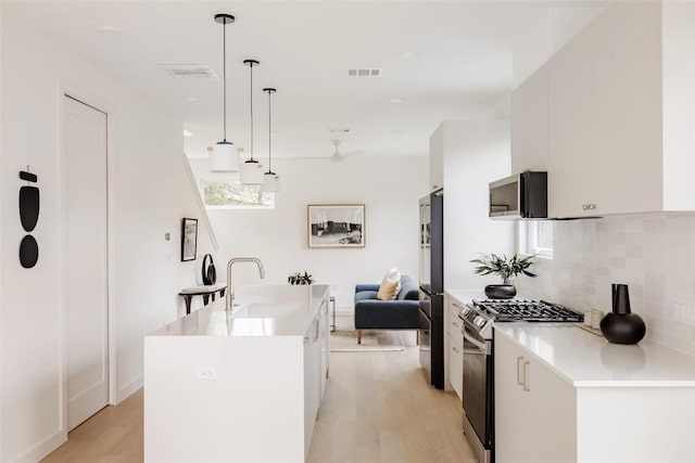 kitchen with white cabinetry, stainless steel range with gas cooktop, pendant lighting, light hardwood / wood-style floors, and a kitchen island with sink