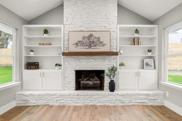 living room featuring a stone fireplace, light hardwood / wood-style flooring, and lofted ceiling