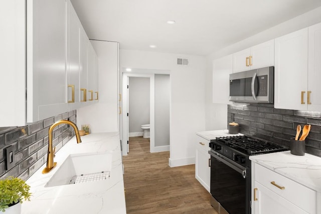 kitchen with light stone countertops, backsplash, stainless steel appliances, sink, and white cabinetry