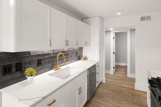 kitchen featuring dishwasher, sink, light stone countertops, tasteful backsplash, and white cabinetry