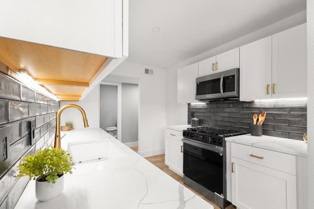 kitchen featuring appliances with stainless steel finishes, white cabinetry, light stone counters, and sink