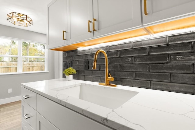 kitchen featuring backsplash, light stone counters, sink, and light hardwood / wood-style floors