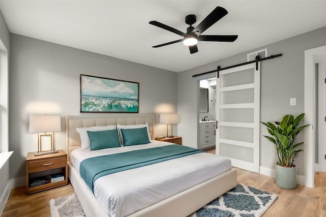 bedroom featuring ceiling fan, a barn door, light wood-type flooring, and connected bathroom