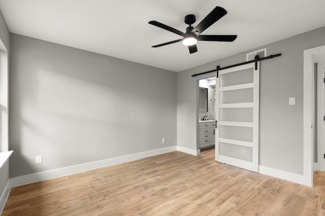 unfurnished bedroom with a barn door, light hardwood / wood-style floors, ensuite bath, and ceiling fan