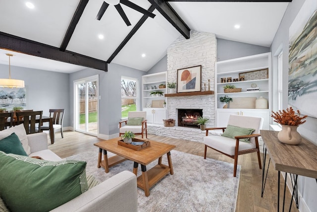 living room featuring ceiling fan, a stone fireplace, beam ceiling, and light wood-style flooring