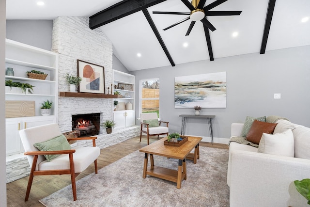 living area with baseboards, a ceiling fan, beamed ceiling, light wood-style floors, and a fireplace