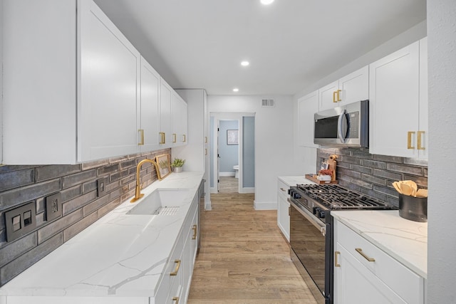 kitchen with white cabinets, stainless steel microwave, light stone counters, gas range oven, and a sink