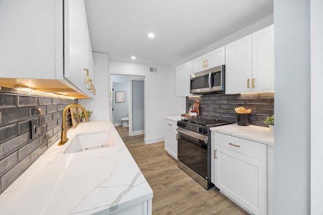 kitchen featuring light wood finished floors, appliances with stainless steel finishes, white cabinetry, a sink, and light stone countertops