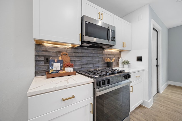 kitchen with light stone counters, tasteful backsplash, light wood-style flooring, appliances with stainless steel finishes, and white cabinets