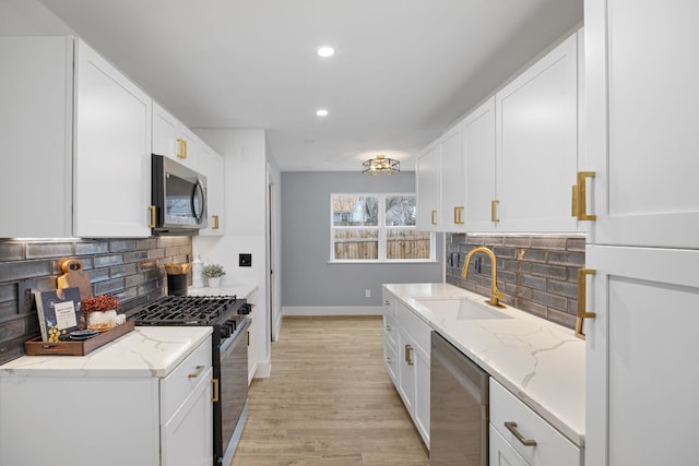 kitchen featuring white cabinets, light stone counters, stainless steel appliances, and a sink