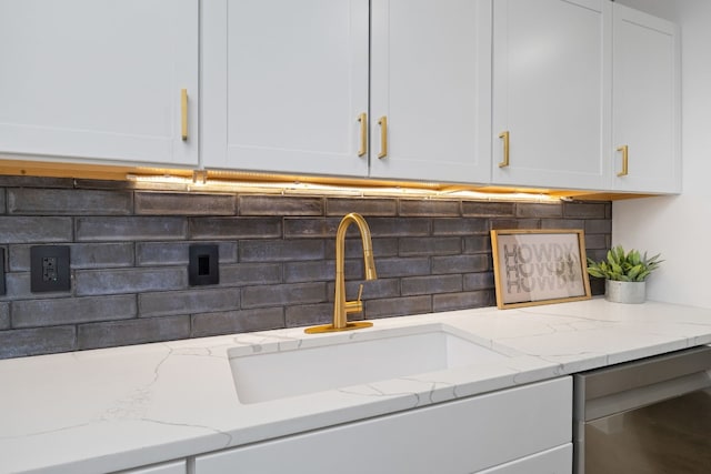 room details featuring light stone counters, backsplash, a sink, and white cabinetry