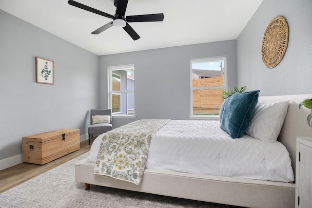 bedroom with ceiling fan, multiple windows, baseboards, and wood finished floors