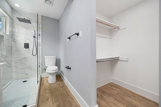 bathroom featuring baseboards, toilet, wood finished floors, a spacious closet, and a shower stall