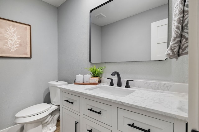 half bathroom with toilet, a textured wall, vanity, and visible vents