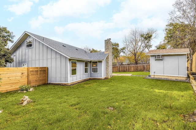 rear view of house with an outbuilding, a fenced backyard, an AC wall unit, a yard, and board and batten siding