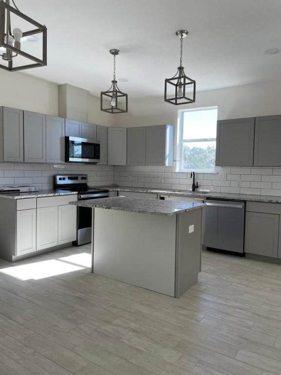 kitchen featuring gray cabinets, a kitchen island, decorative light fixtures, and appliances with stainless steel finishes