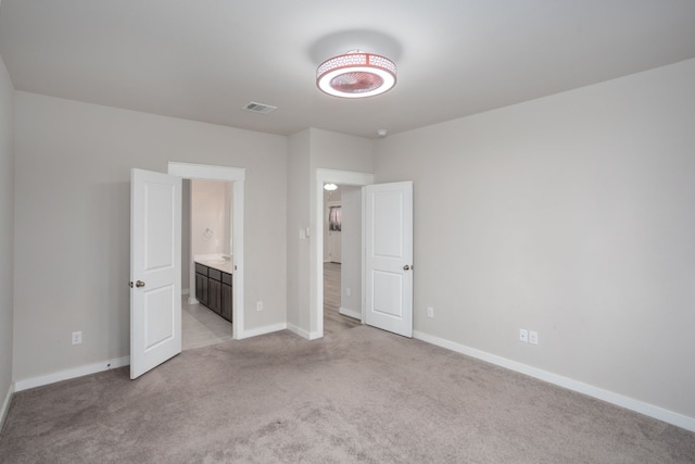 unfurnished bedroom featuring light colored carpet and ensuite bath