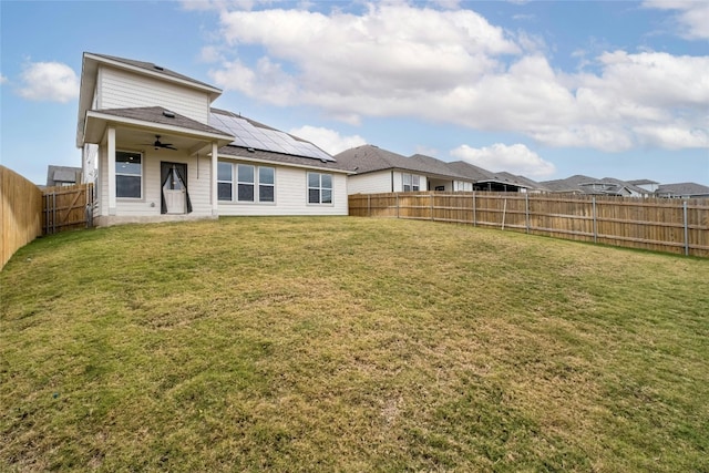 rear view of house featuring solar panels, ceiling fan, and a lawn