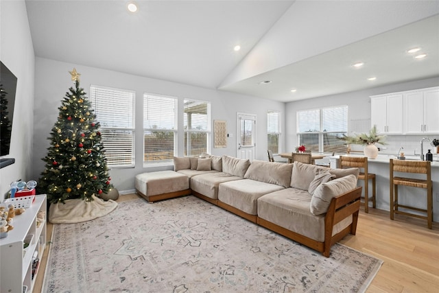 living room with sink, vaulted ceiling, and light wood-type flooring