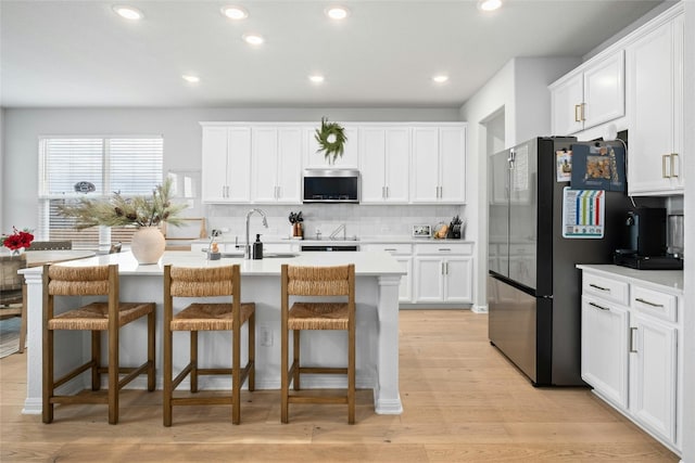 kitchen featuring a kitchen breakfast bar, a center island with sink, white cabinets, and stainless steel appliances