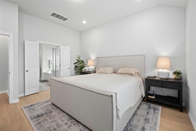 bedroom with light wood-type flooring, ensuite bath, and lofted ceiling