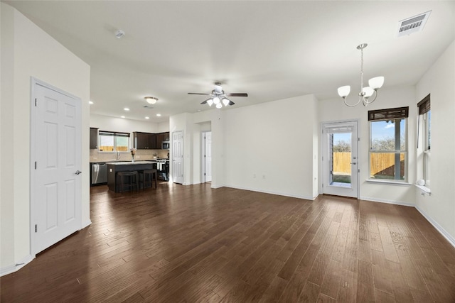 unfurnished living room with ceiling fan with notable chandelier, dark hardwood / wood-style flooring, and plenty of natural light