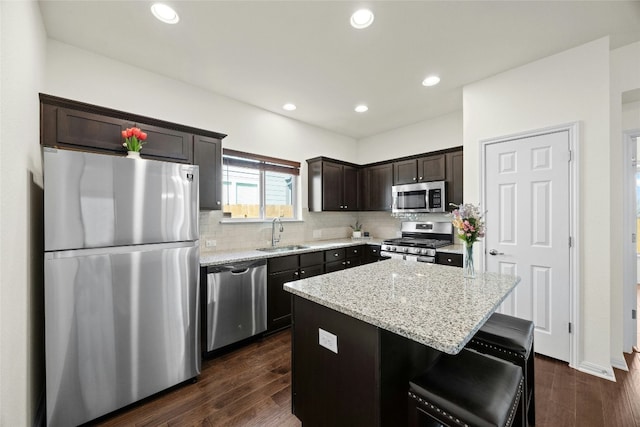 kitchen featuring a center island, sink, dark hardwood / wood-style floors, light stone counters, and stainless steel appliances