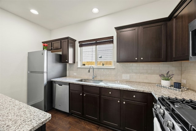 kitchen with sink, dark hardwood / wood-style floors, light stone countertops, dark brown cabinetry, and stainless steel appliances