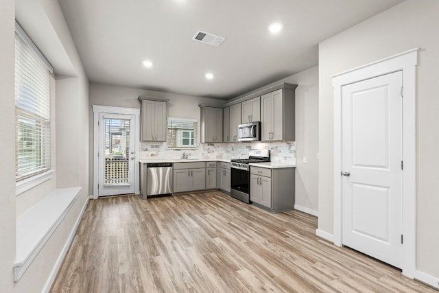 kitchen with light wood-type flooring, stainless steel appliances, gray cabinets, and tasteful backsplash