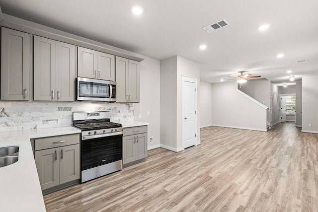 kitchen featuring ceiling fan, stainless steel appliances, gray cabinets, decorative backsplash, and light wood-type flooring