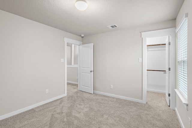 unfurnished bedroom with multiple windows, a walk in closet, light carpet, and a closet