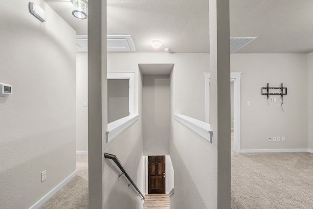 stairway with carpet floors and a textured ceiling