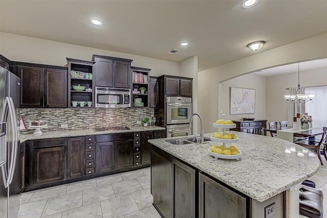 kitchen featuring light stone counters, stainless steel appliances, sink, a chandelier, and an island with sink