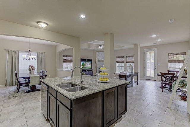 kitchen featuring light stone countertops, dishwasher, sink, an island with sink, and dark brown cabinets