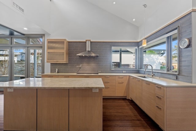 kitchen featuring light brown cabinetry, tasteful backsplash, wall chimney range hood, sink, and a center island