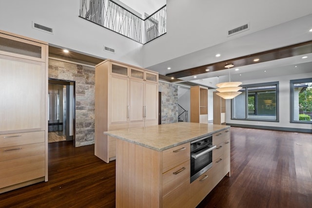 kitchen featuring light brown cabinetry, a kitchen island, oven, and decorative light fixtures