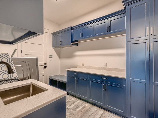 kitchen with blue cabinetry, light stone counters, sink, and light wood-type flooring