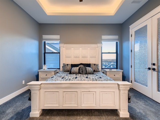 bedroom with a raised ceiling, french doors, and dark colored carpet