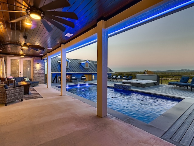 pool at dusk with an outdoor living space, pool water feature, ceiling fan, a patio area, and a hot tub