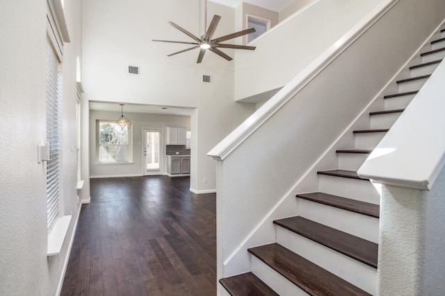 stairway with hardwood / wood-style floors, ceiling fan with notable chandelier, and a towering ceiling