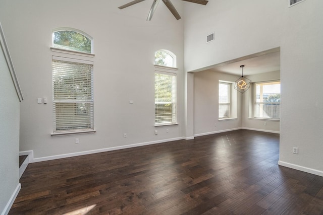 unfurnished living room with a towering ceiling, dark wood-type flooring, and ceiling fan with notable chandelier