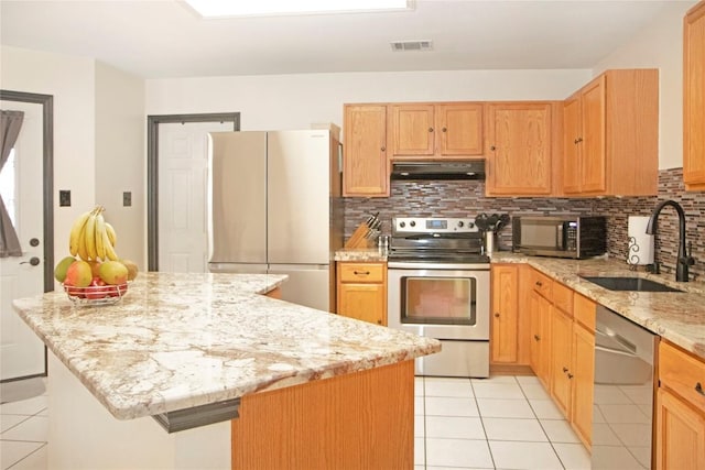 kitchen with appliances with stainless steel finishes, light stone counters, sink, light tile patterned floors, and a center island