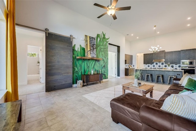 living area with a barn door, light tile patterned flooring, recessed lighting, ceiling fan with notable chandelier, and a high ceiling