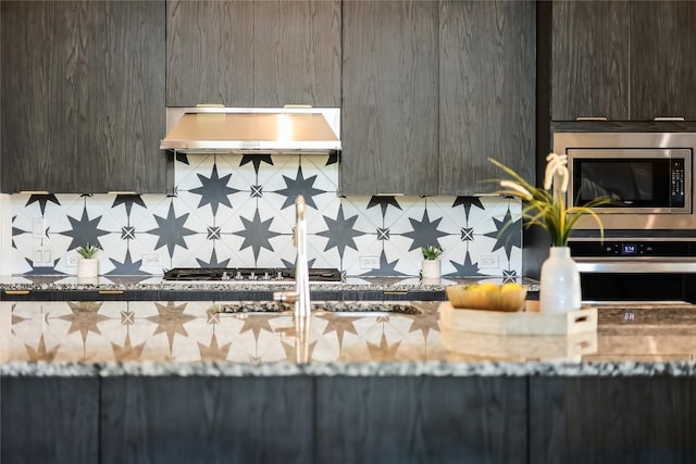 kitchen with stone countertops, under cabinet range hood, stainless steel appliances, decorative backsplash, and modern cabinets